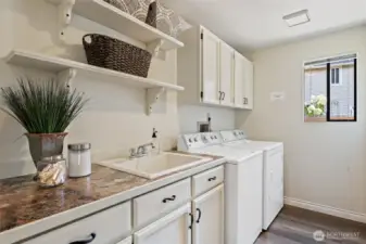 Main floor laundry room with built-in cabinets, sink, shelving, and washer and dryer included.
