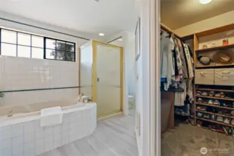 Soaking tub, shower, and walk-in closet with built-in shelving.