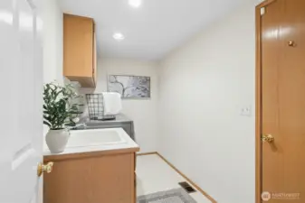 Utility room with a sink and cabinets and a door leading out to the large 3-car garage.