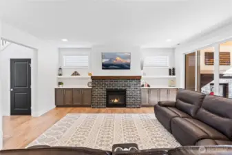 Living room showcases brick-framed gas fireplace and custom built in cabinetry.