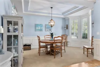 Formal dining room with same tray ceiling and wainscoting detail, crown molding and bay window with custom plantation shutters.
