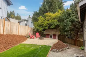 Backyard with fresh sod, fire pit, and shed for tools and path down to lower patio and hot tub.