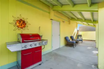 Outdoor covered patio with metal roof, and just beyond the patio is a big shed with gravel behind it and another large fence gate.