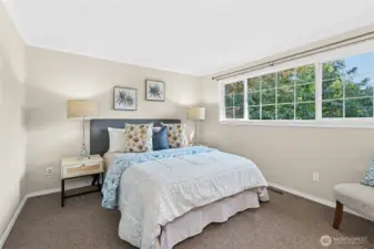 Primary suite with carpeted floor and large window overlooking the backyard is a peaceful retreat in this Kirkland home.