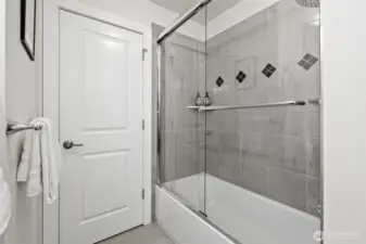 A tiled shower-tub combo with glass enclosure and accent detailing completes the full main-level bath—perfect for guests or everyday use.