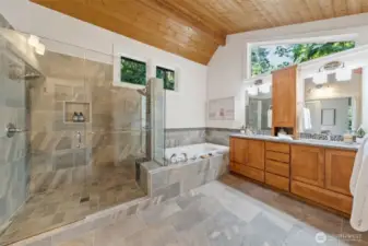 Indulge in the luxury of a double showerhead walk-in shower with frameless glass, pebble-tile accents, and a jetted soaking tub—all framed by peaceful forest views that bring the outside in.