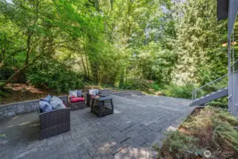 Surrounded by lush greenery and creek, this expansive paver patio offers a peaceful escape—perfect for evening conversations around the fire table or morning coffee in the shade.