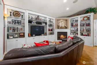 The family area with hardwood flooring and vaulted ceiling adds to the open concept feeling complete with custom floor to ceiling built-ins and a cozy gas fireplace
