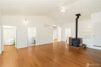 Enjoy open floor plan w/ vaulted ceilings and plenty of natural light. Office is shown on the left (with white chair), laundry, guest bedroom and door to entry. Stairs are behind wood burning stove.