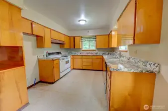 Kitchen with updated counter tops, vintage stove/range and black dishwasher across the kitchen. Sink is located next to the dishwasher. Refrigerator cutout space in cabinetry next to the stove.