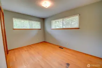 Primary bedroom on main floor with hardwood floors, closet and two corner windows.