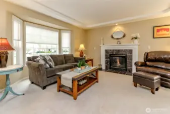 The cozy living room is bathed in natural light from the large windows. The centerpiece of the room is a beautiful gas fireplace.