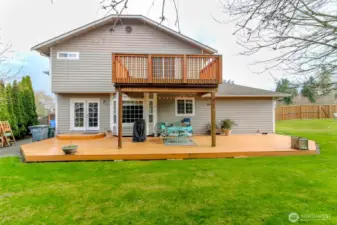A rear facing view of this beautiful home with a sprawling, expansive backyard that feels private and inviting. The backyard is fully fenced, ensuring a safe , secluded outdoor space. A large deck on the main floor extends from the back of the home, perfect for outdoor dining and entertaining, while a generous sized deck extends off the primary bedroom upstairs. The landscape features lush mature greenery adding to the sense of privacy.