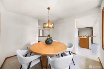 Inviting dining space with seamless flow into the kitchen, highlighted by a central light fixture, updated neutral carpet, and a spacious layout perfect for everyday meals or entertaining. Natural light enhances the warm wood accents and open feel.