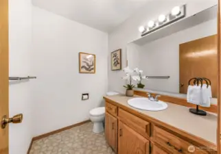 Convenient half bath on the main floor includes a wide vanity with oak cabinetry, large mirror, and decorative lighting. Ideal for guests and day-to-day use.