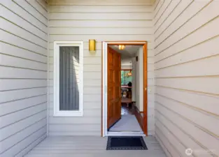 Covered front entry with wood-paneled siding and a warm wood front door offers a welcoming first impression, enhanced by a modern exterior light fixture and clean-lined trim.