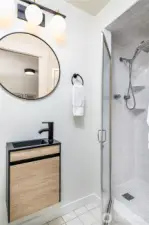 Primary ¾ bath designed for efficient use of space, featuring a charming compact sink on the left and a spacious shower on the right.