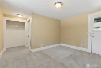 This is Unit A's main floor primary bedroom with the closet just ahead next to the 3/4 bathroom. The exterior door out the back deck is to the right.
