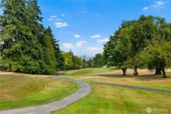 Expansive fairways framed by towering evergreens, with the Seattle skyline shimmering in the distance.