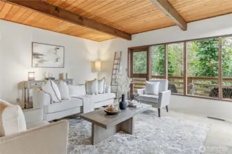 The large living room with a wall of windows facing a beautifully wooded ravine.