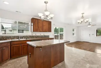 Looking across the kitchen, you get the full effect, with a no-fuss neutral Formica countertop on the island with a corner-clipped design to avoid any head-bonking from kids doing laps. The big window over the sink, the dining area with its chandelier, the sliding glass door to the deck, even the front door and living room windows all line up to show the great room flow.