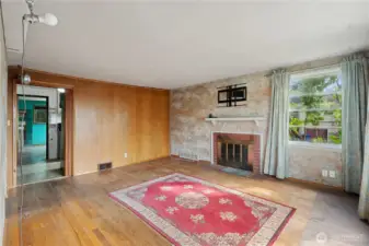 Living room with original hardwood flooring, wood-burning fireplace and wood-paneling details.