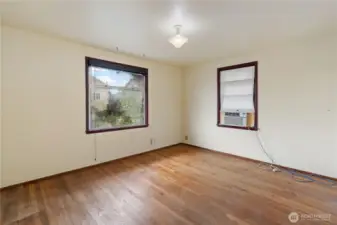Bedroom #2 down the hallway with hardwood flooring, a window overlooking the front yard and a portable A/C unit.