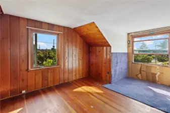 On the other side of the hallway is Bedroom #5 with hardwood flooring, wood paneling details and large windows.