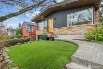 Striking modern exterior with bold vertical siding, warm stone accents, and a vibrant front door that makes an unforgettable first impression. The curved walkway and manicured turf create a clean, low-maintenance approach, framed by mature trees for added character and privacy.