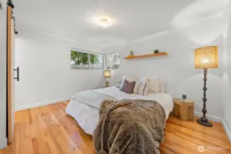 Welcome to the Primary Suite featuring hardwood floors, clean architectural lines, and a sliding barn door detail that adds modern character. Corner windows introduce natural light while maintaining privacy and tranquility.