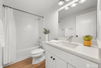Lower-level main bathroom featuring a full tub with subway tile surround, quartz vanity, and modern fixtures