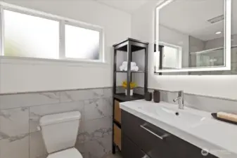 Marble-style tile, modern fixtures, and a backlit mirror elevate the ensuite bathroom experience.