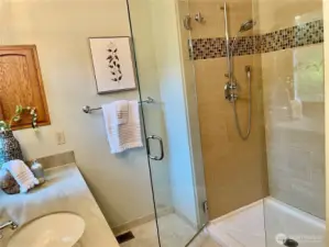 The primary bathroom shower is designed with a sleek, frameless glass door that enhances the space with an open, modern aesthetic.