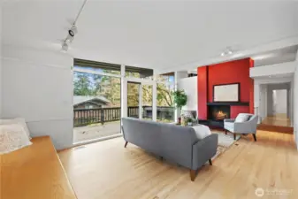 Bright living room with original hardwood floors, wood-burning fireplace, and dramatic walls of windows. Designed for natural light and seamless indoor-outdoor living.