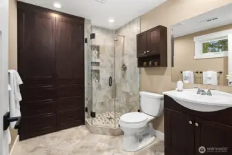 The en suite 3/4 bath is adorned with tile floors, shower, a frameless glass panel shower door, and a large built-in cabinet.