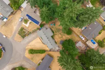 This direct overhead aerial shot showcases the full property layout, highlighting the spacious lot, mature trees providing natural privacy, and the home’s position on a quiet cul-de-sac. The fenced backyard, circular fire pit area, and generous driveway offer a clear view of the home's outdoor features and functionality.