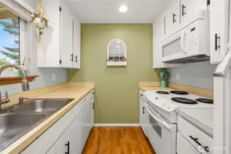 This view showcases the kitchen's layout, featuring a white electric range with a matching microwave above. The fresh green accent wall adds warmth and frames the decorative pass-through shelf at the end of the space.