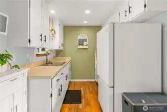 An extended view down the galley kitchen emphasizes the continuous cabinetry and countertop workspace. Overhead recessed lighting and a thoughtful layout create a clean, organized flow for daily meal prep and storage.
