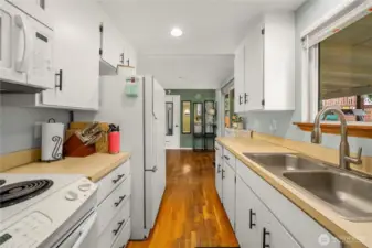 Looking from the kitchen toward the dining area, this angle highlights the hardwood floors and ample cabinet storage on both sides. Sliding glass doors to the right offer easy access to the covered patio—perfect for indoor-outdoor entertaining.