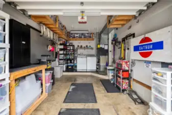 This well-maintained single-car garage offers both secure parking and ample workspace. Overhead and wall-mounted shelving provide smart storage solutions, while pegboard walls and open shelving make organization easy. At the rear, a dedicated laundry area features a side-by-side washer and dryer, a folding shelf, and utility hookups, all conveniently located near the home’s mechanical systems.