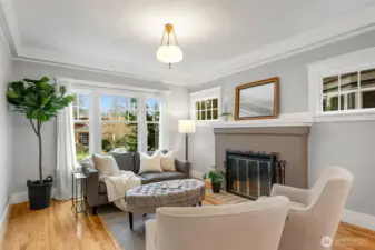 The living room features high ceilings,  original wood windows, the original tile  fireplace, and detailed millwork.