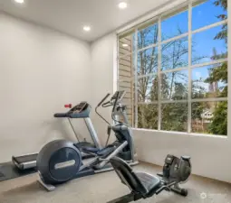 A bright and airy third-floor exercise room with expansive windows offering serene views of a lush landscape below.