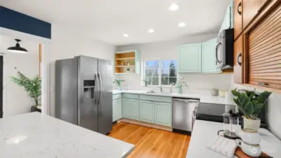 Kitchen features stainless steel appliances, recessed lighting, light cabinetry, open shelving detailing and window above the sink.