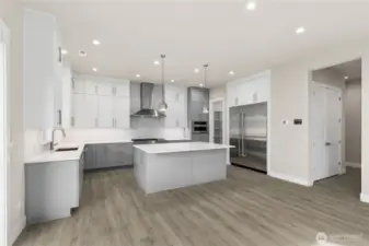 Chef-inspired kitchen with a large center island, custom two-tone cabinetry, commercial-style range hood, double ovens, and a built-in fridge. Bright, modern finishes and ample storage make this space both functional and stunning.