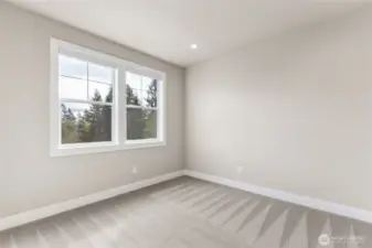 Secondary bedroom with soft neutral tones, large windows framing treetop views, and plush wall-to-wall carpeting. A bright and peaceful space ideal for guests, a home office, or a nursery.