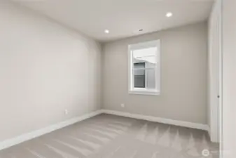 Cozy bedroom with soft neutral tones, plush carpeting, and recessed lighting. A large window provides natural light and a peaceful setting—perfect for a guest room, office, or additional sleeping space.
