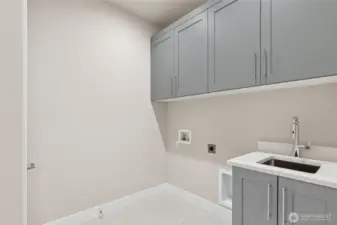 Well-appointed laundry room featuring upper and lower cabinetry for storage, a deep utility sink with modern faucet, and dedicated hookups for washer and dryer. A bright, efficient space designed for everyday convenience.