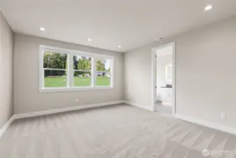 Spacious primary bedroom featuring plush carpet, recessed lighting, and a wall of windows that fill the room with natural light and peaceful backyard views. Includes direct access to a private en-suite bath.