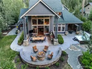 This close-up drone view reveals the thoughtfully designed outdoor experience: a covered outdoor kitchen and dining space, curved firepit lounge with built-in seating, and spa area just off the primary suite — every inch crafted for luxury and connection.