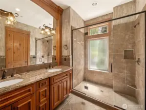 Spa-inspired bathroom offers double vanities with granite counters, under-mount sinks, designer light fixtures, and custom cabinetry. The oversized walk-in shower is beautifully tiled with a frameless glass enclosure, built-in shelving, and natural light streaming through a frosted privacy window.